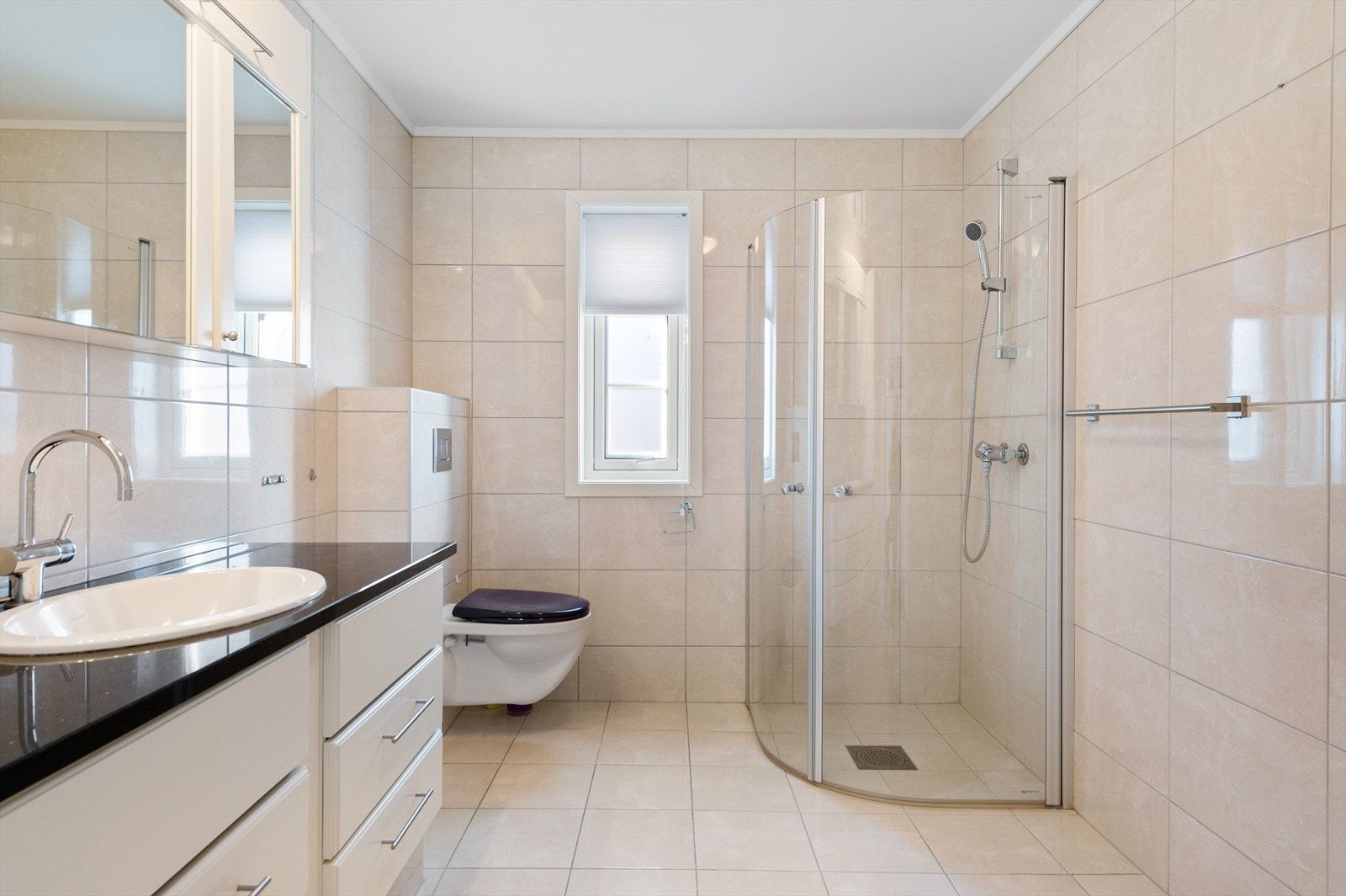 Tidløst og pent bad med dusjhjørne, veggmontert toalett og innredning med servant Galleribilde