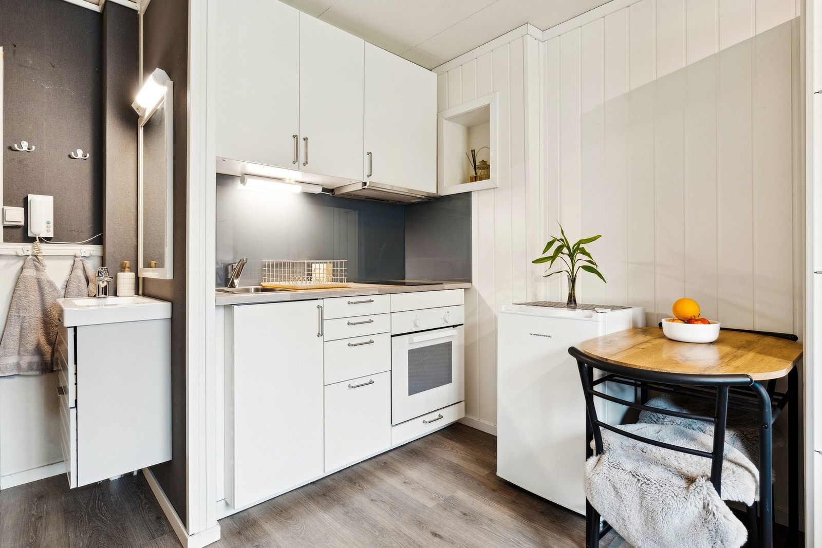 Hybelkjøkken med nedfelt vask, stekeovn, induksjonstopp og frittstående kjøleskap. Sevantinnredning på vegg. Galleribilde