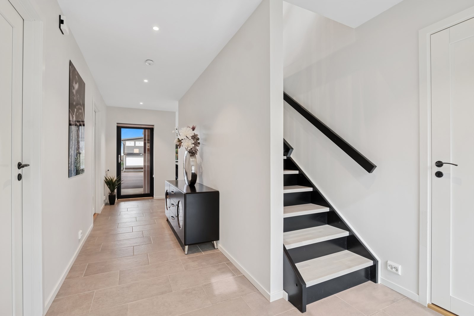 Innenfor hovedinngangen møtes man av en lys og romslig hall som strekker seg videre innover boligens 1. etasje, med flislagt gulv med varmekabler. Her er det enkelt og hyggelig å ønske gjester velkommen inn! Galleribilde