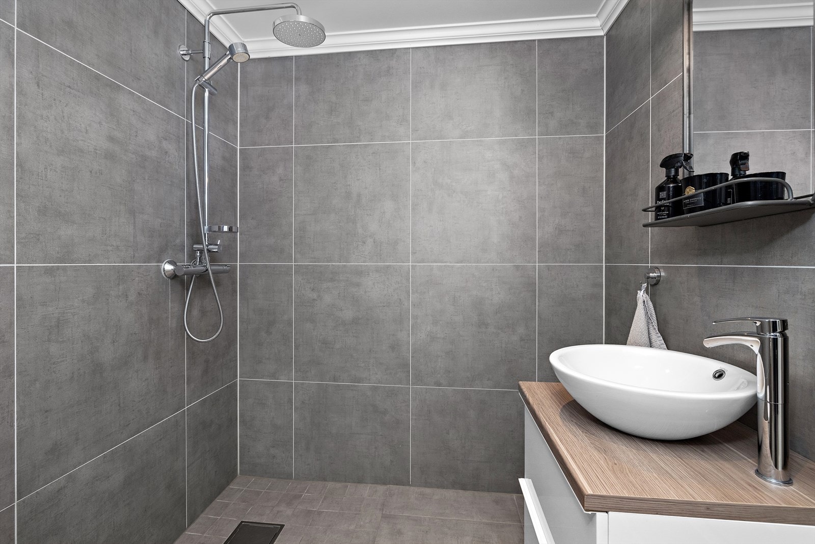 Badet er innredet med hvit baderomsinnredning med bolle servant og rom for oppbevaring i underskap. Videre er badet utstyrt med dusjhjørne, speil og vegghengt toalett. Galleribilde