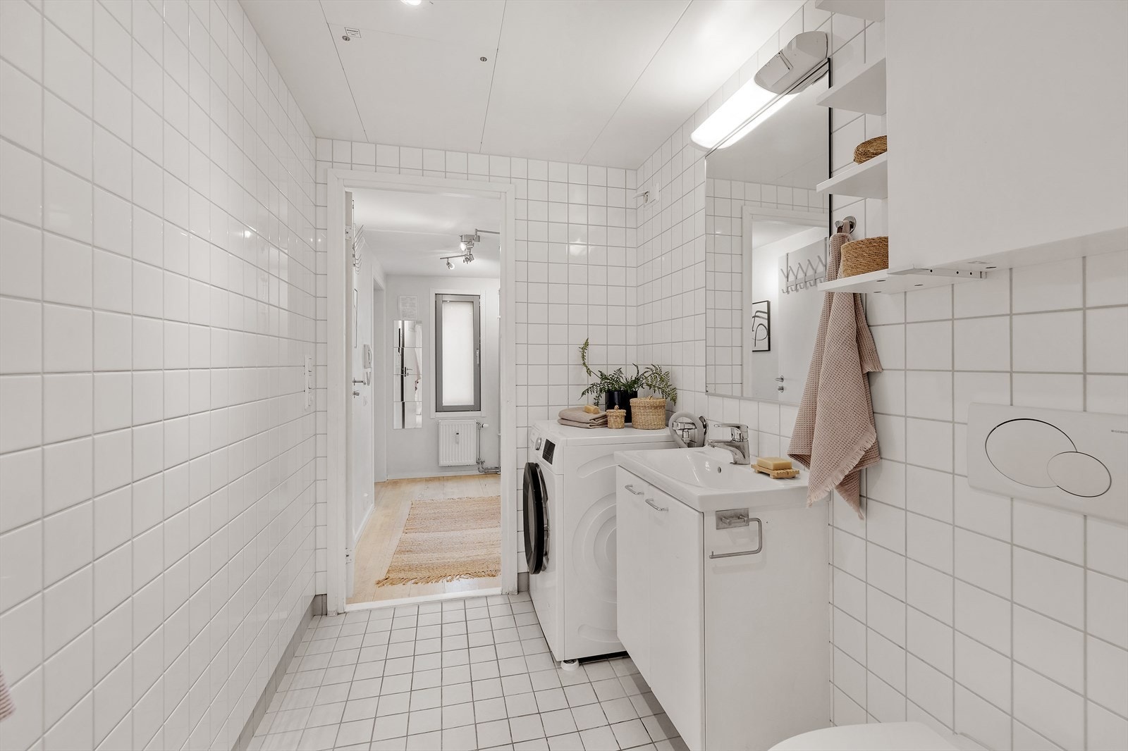 Romslig baderomsinnredning med heldekkende servant nedfelt i underskap, speil m/lys, veggmontert toalett, dusjhjørne m/glassdører og opplegg for vaskemaskin. Galleribilde