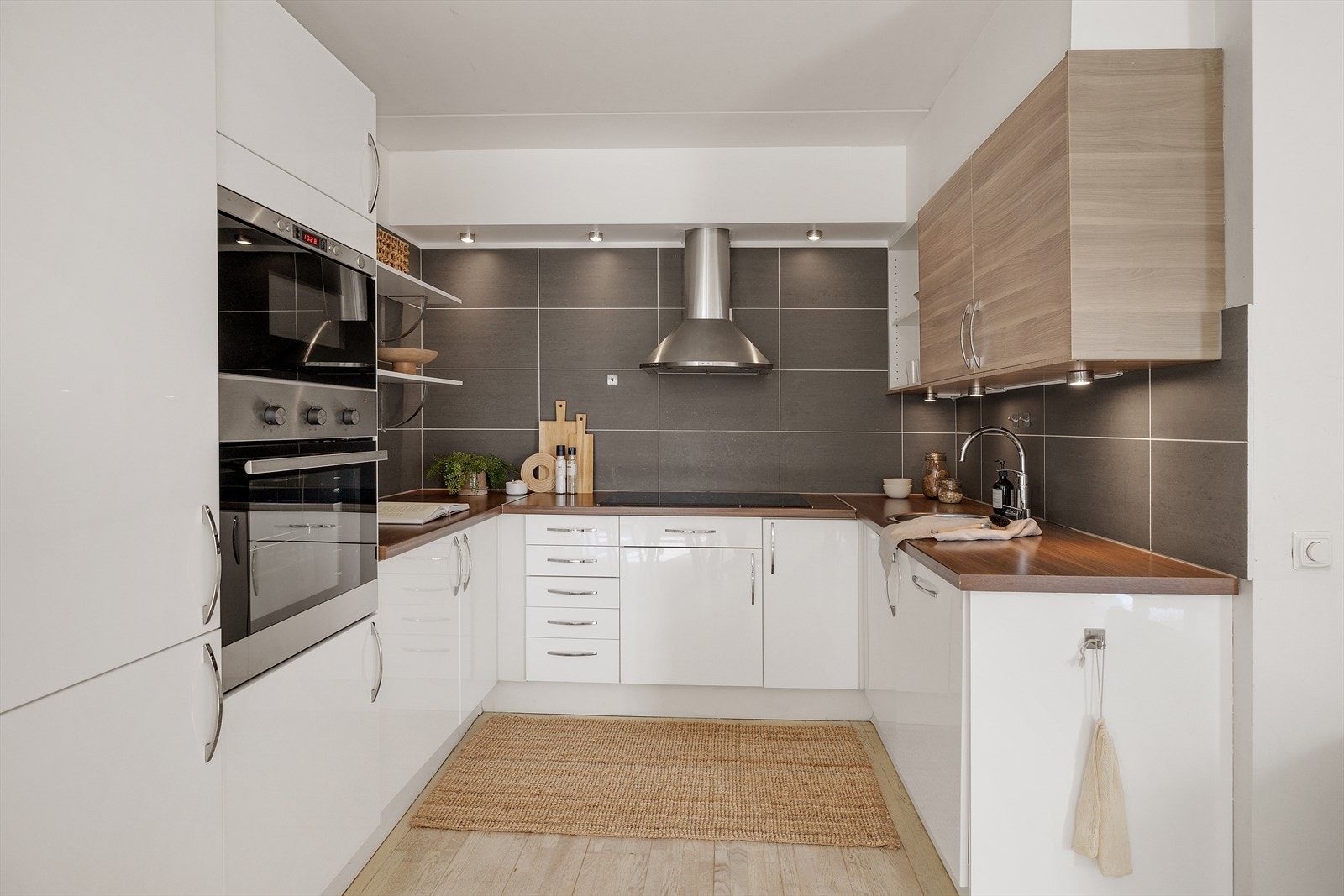 Lekker kjøkkeninnredning med glatte fronter, laminert benkeplate, oppvaskkum, ventilator og fliser over benk. Galleribilde