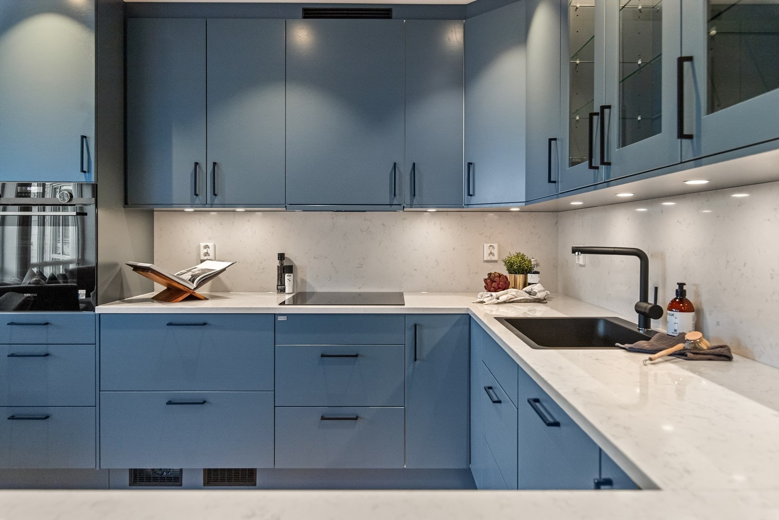 Innredningen er fra Huseby av typen Pesto , med vitrineskap, sorte håndtak og glatte fronter i en mørk blåtone. Galleribilde