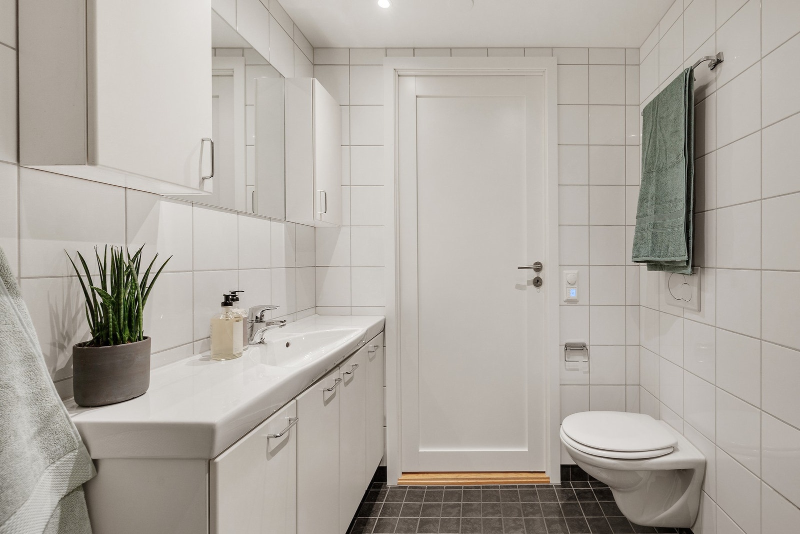 Badet har vegghengt servantskap, overskap, vegghengt toalett, dusjdører i glass og opplegg for vaskemaskin Galleribilde