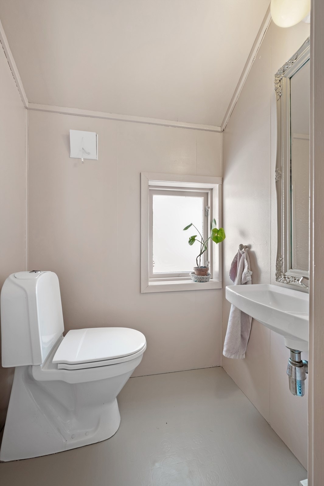 Toalettrommet i leiligheten er lyst og pent med servant, toalett, vinylbelegg og vindu. Galleribilde
