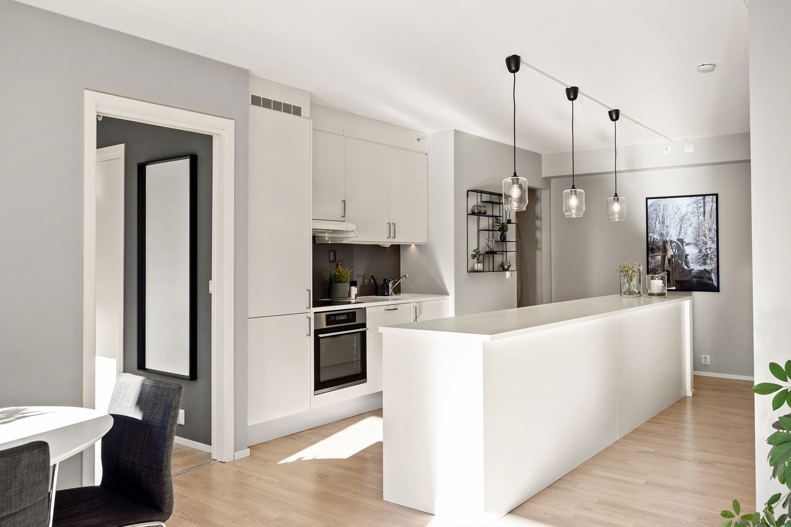 Kjøkkeninnredningen har hvite, glatte fronter og benkeplate i laminat. Nedfelt oppvaskkum i antrasitt med ettgreps svingbart blandingsbatteri. Backsplash i måltilpasset glass, i samme fargeserie som stuen (Altigalss), skaper et helhetlig design. Galleribilde