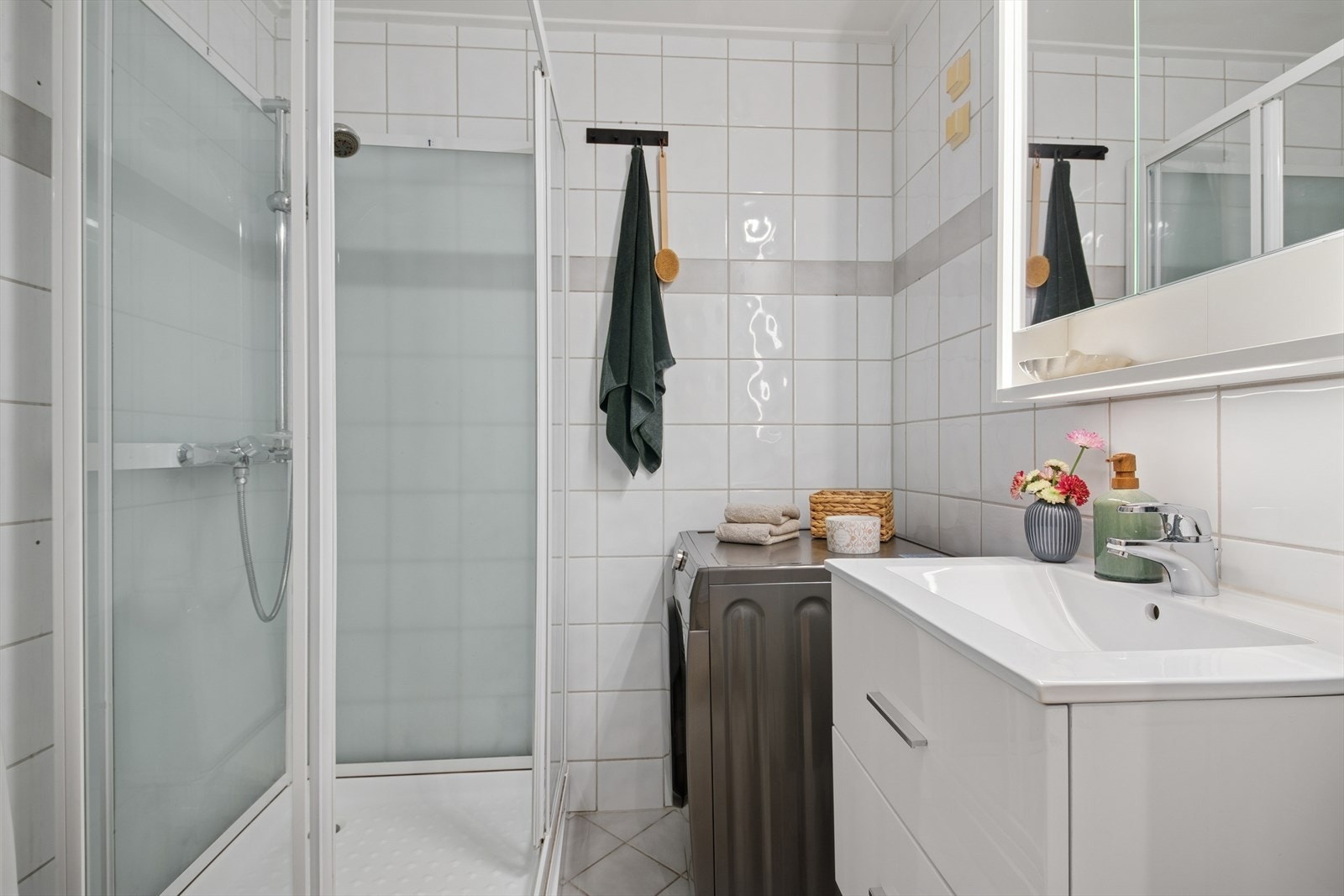 Badet er innredet med gulvmontert toalett, servant med servantskuffer, overskap med speilfronter fra 2025, dusjkabinett og opplegg for vaskemaskin Galleribilde