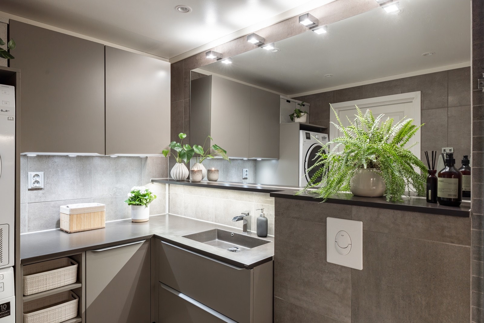 Stilren og flott baderomsinnredning med glatte fronter i en fin farge og benkeplate i kompositt med helstøpt nedfelt servant med fossefall armatur. Praktisk hylle over servanten med stort speil og vegghengt belysning over. Galleribilde