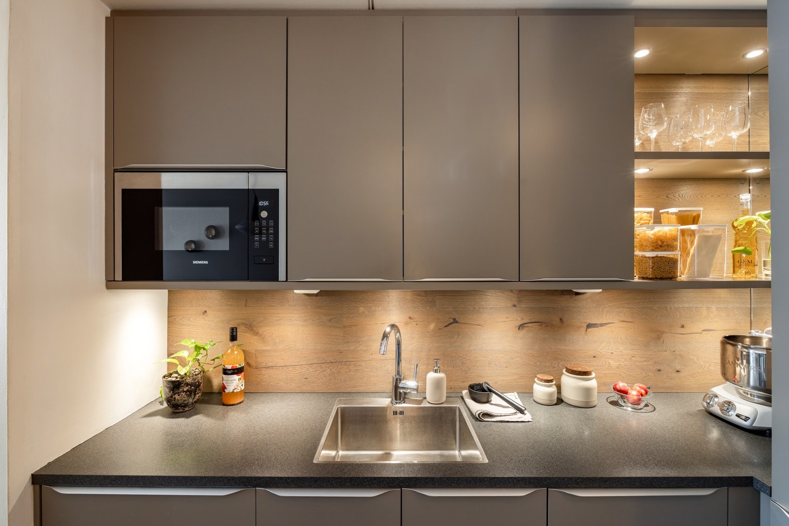 Moderne innredning med glatte fronter i mørk sand og laminert benkeplate med planlimt oppvaskkum. Praktisk med belysning under de takhøye overskapene. Galleribilde