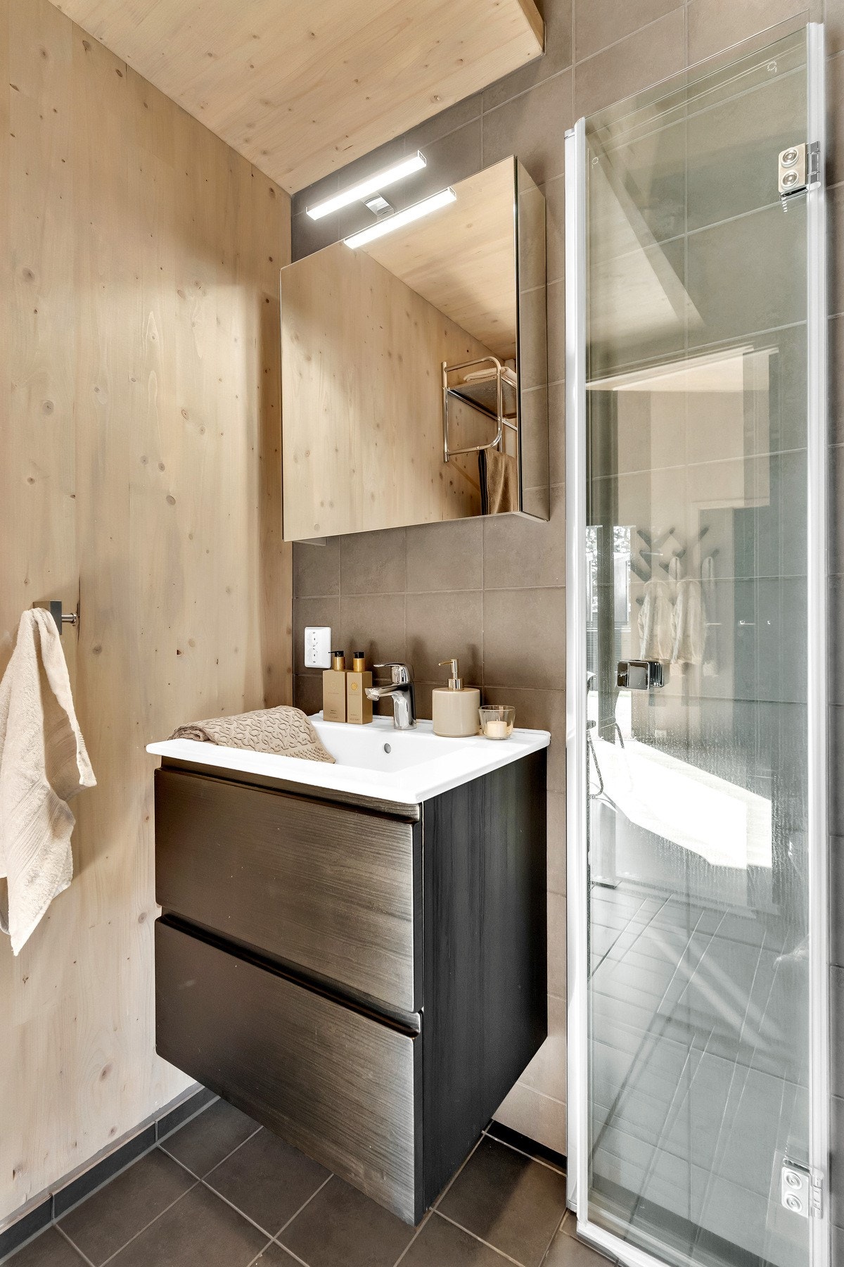 Badet er utstyrt med vegghengt innredning med skuffer og servant med ett-greps armatur, vegghengt toalett og dusjhjørne med foldbare dører og ett-greps armatur med hånddusj. Galleribilde