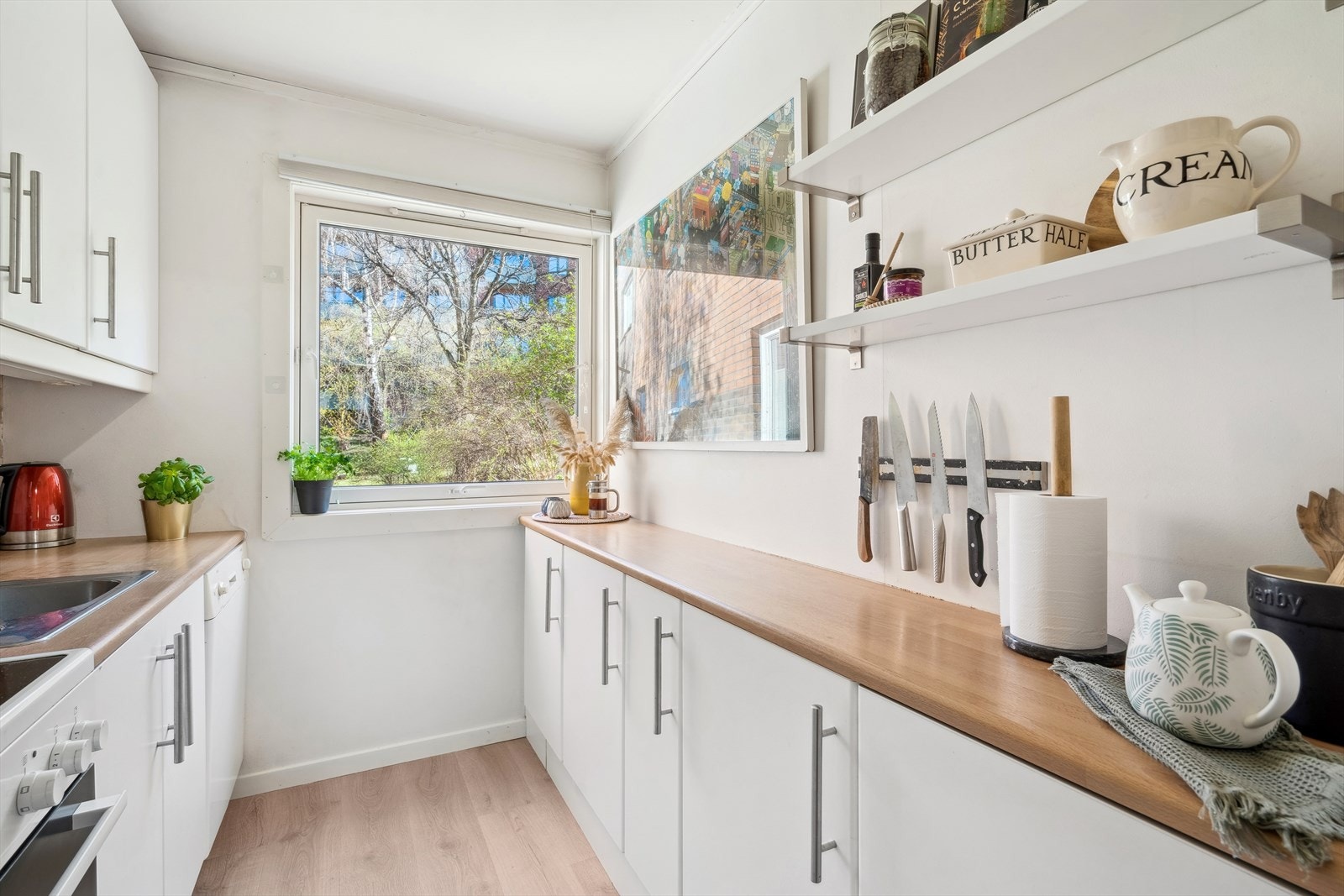 Kjøkkeninnredning med hvite og slette fronter. Fliser og lys over laminat benkeplate med nedfelt oppvaskkum. Galleribilde