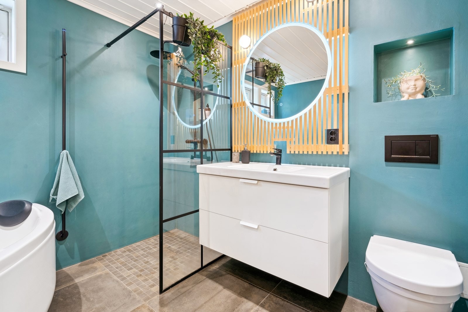 Innredningen består av servant med hvitt underskap, speil med lys som er festet på spilevegg og strømuttak. Videre er det regnfallsdusj med glassdør, stor hjørnebadekar, vegghengt toalett og god plass vaskemaskin og tørketrommel. Galleribilde