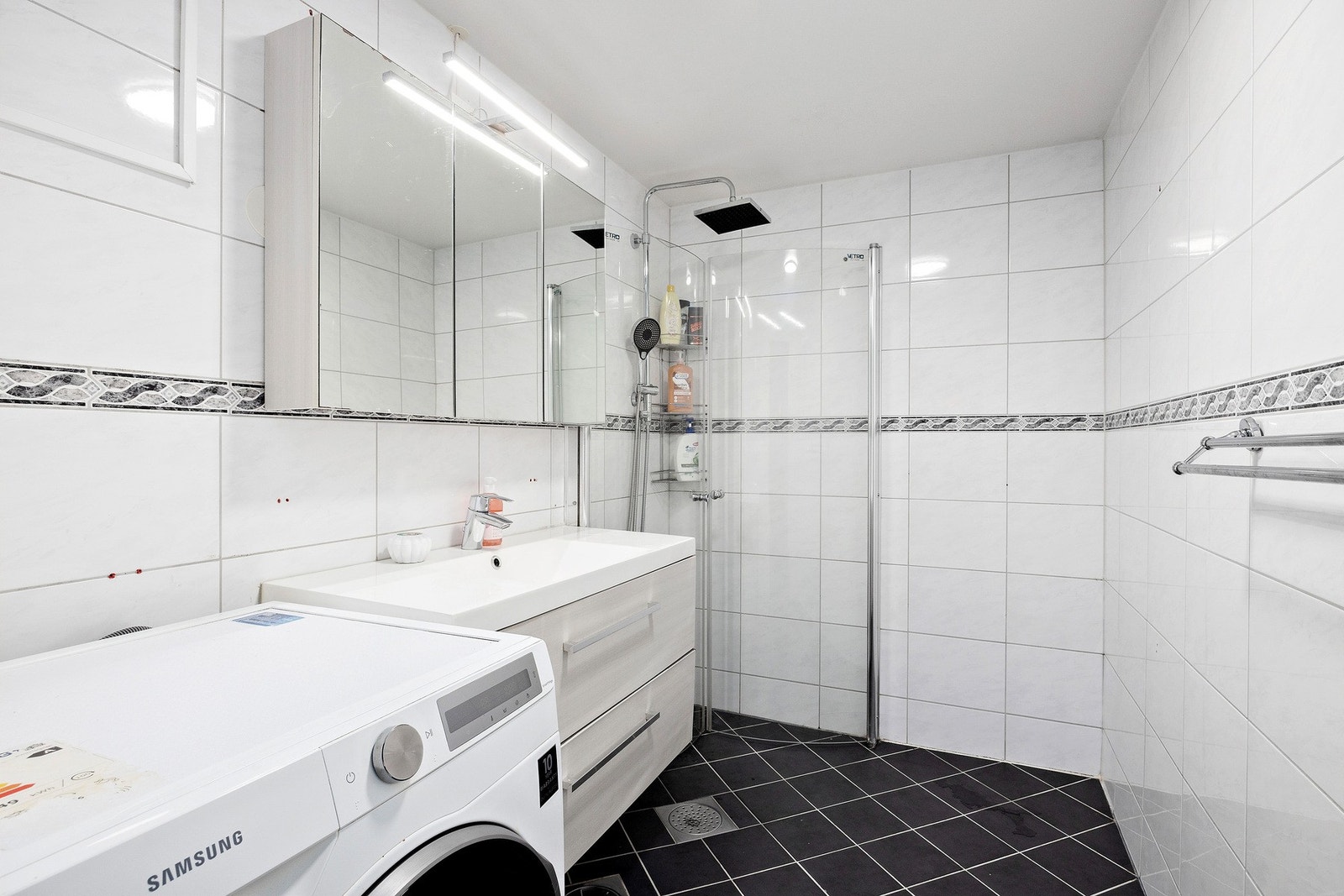 Badet ble renovert i 2012 og fremstår pent med fliser på både gulv og vegger. Det er varmekabler i gulvet for ekstra komfort, og innredningen består av nedfelt servant, dusjhjørne og opplegg for vaskemaskin. Galleribilde