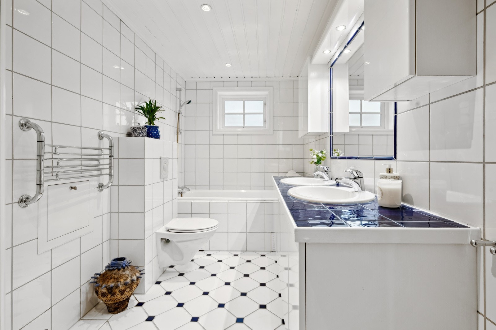 Badet er innredet med servanter, innmurt speil, overskap med belysning, dusjhjørne med innfellbare glassdører og regnfallsdusj, badekar, samt vegghengt toalett. Galleribilde