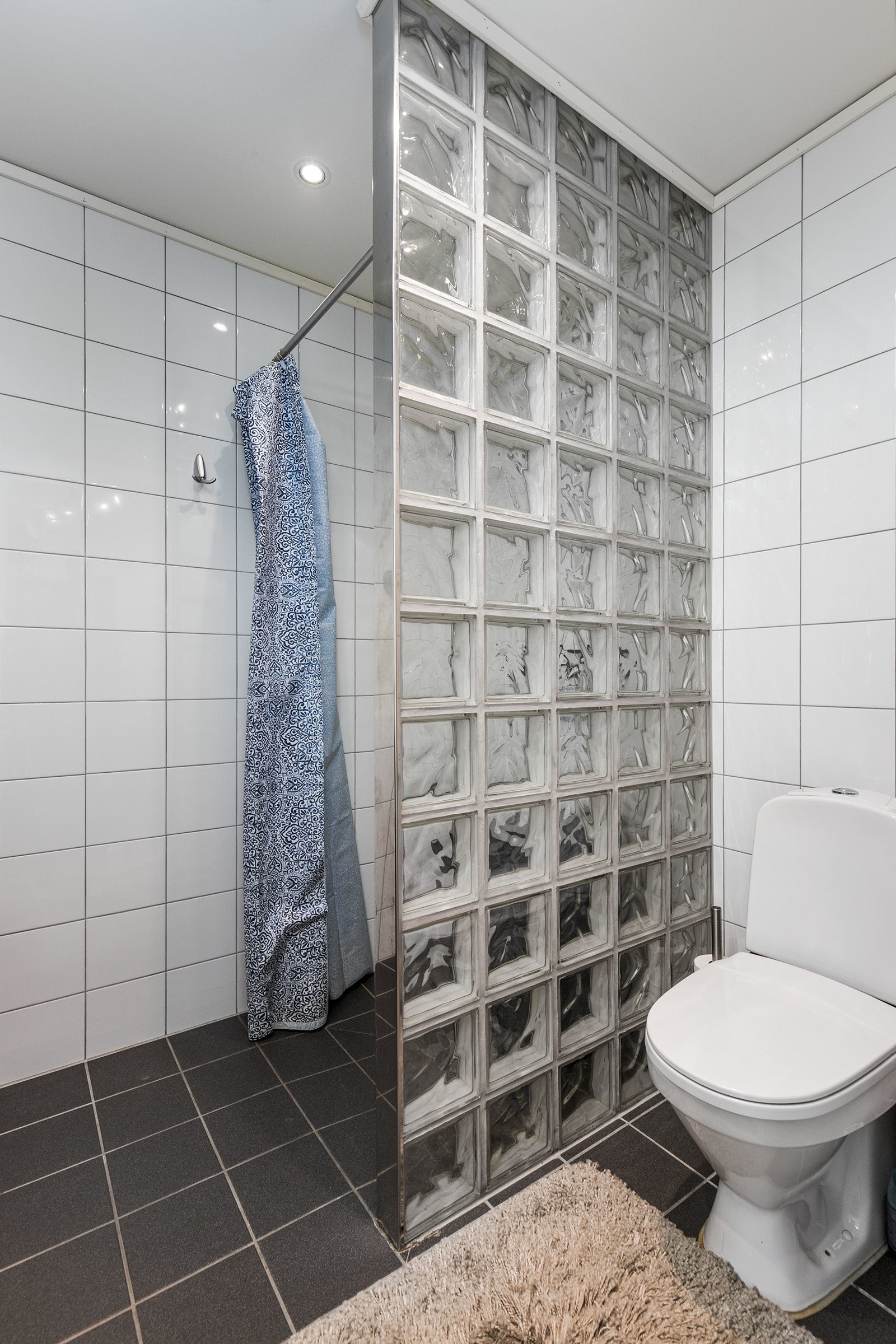 Videre har badet dusj på gulv og vegg med glassbyggerstein, gulvstående klosett, servant og opplegg for vaskemaskin. Galleribilde