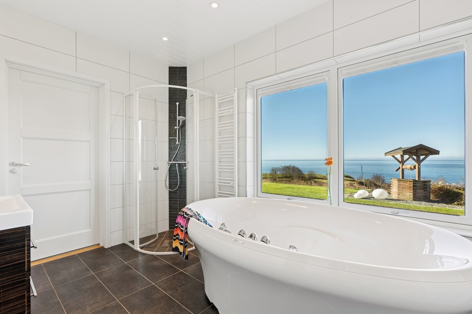 Et pent bad som inneholder speil med belysning, servant med seksjon, dusjhjørne, massasjebadekar fra Hurricane og veggmontert toalett. Galleribilde