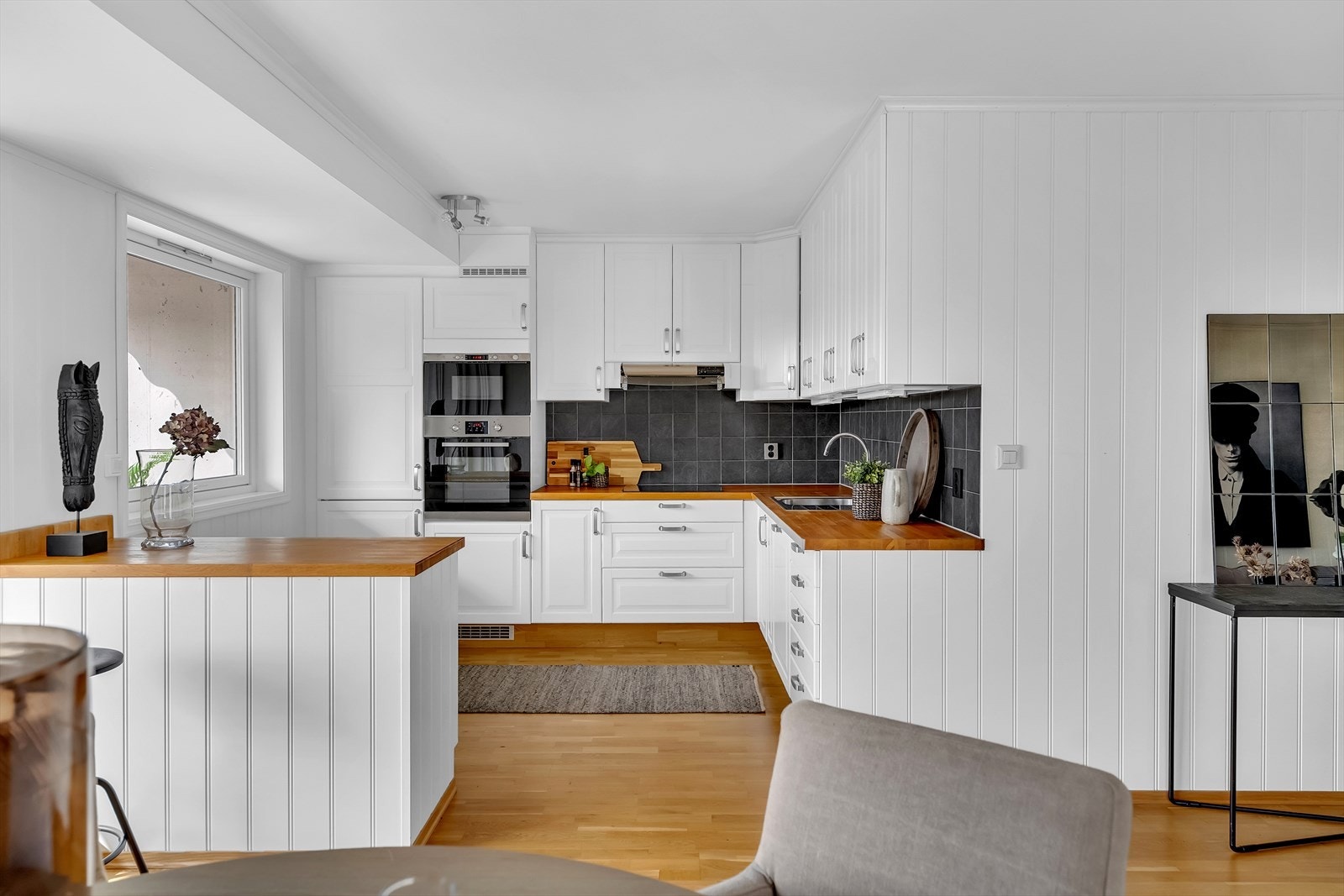 Lyst og pent kjøkken i tidløst uttrykk med åpen løsning mot stuen med kjøkkenøy. Galleribilde