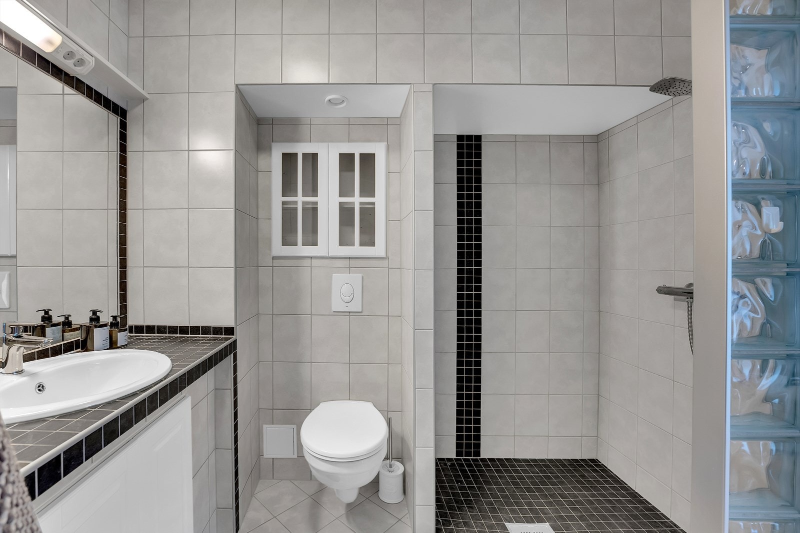 Baderommet har dusjnisje med glassbyggerstein og nisjer til toalett, innredning og vaskemaskin. Galleribilde