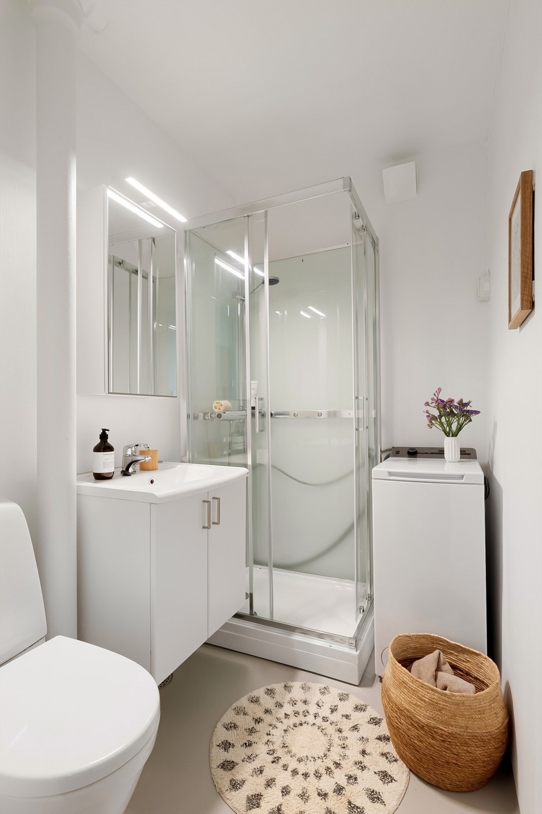 Badet har overskap med speil, dusjkabinett, gulvmontert toalett og opplegg for vaskemaskin Galleribilde