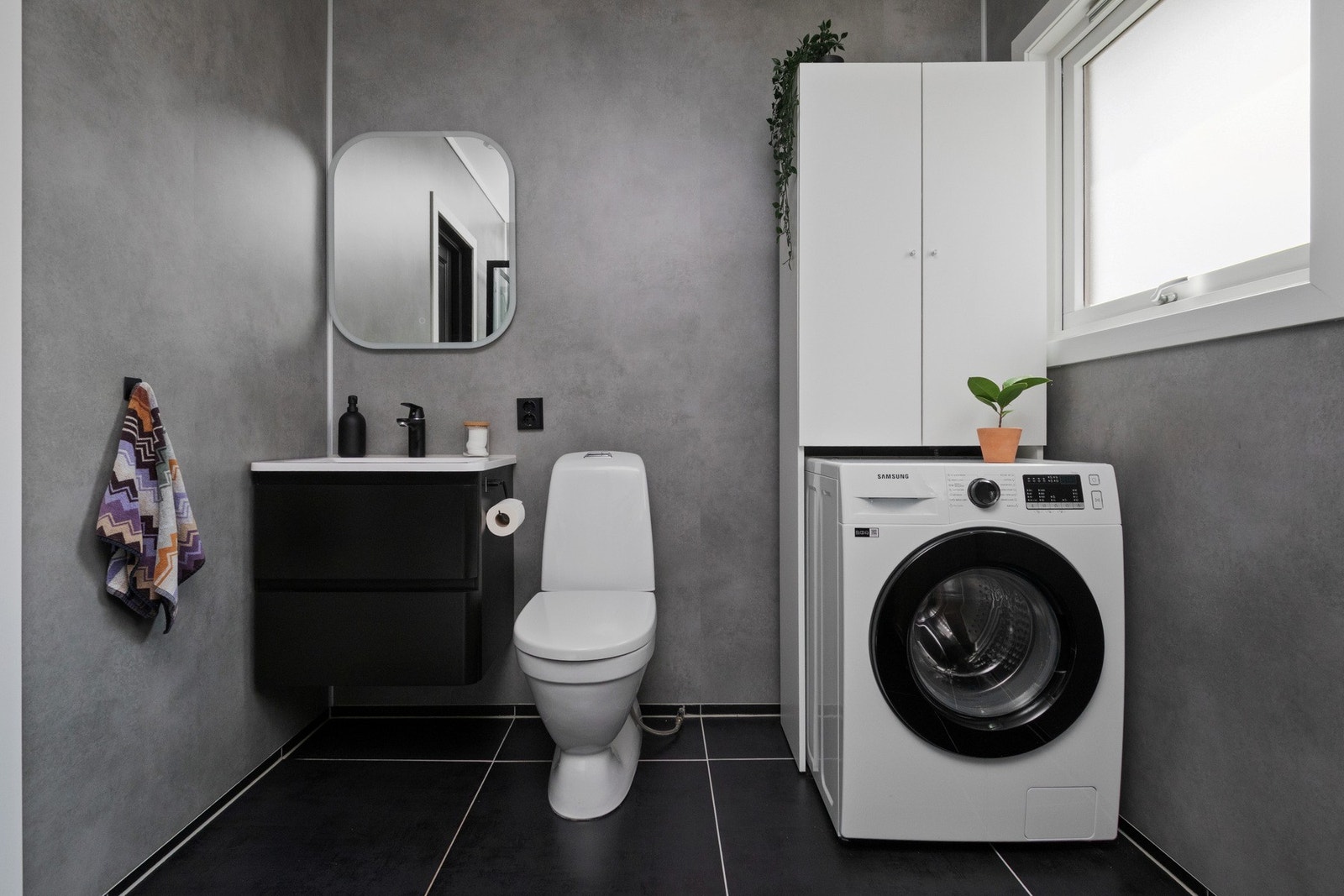 Den øvrige innredningen består av en servant med sorte skuffer, et hvitt høyskap og et speil med integrert belysning. Galleribilde