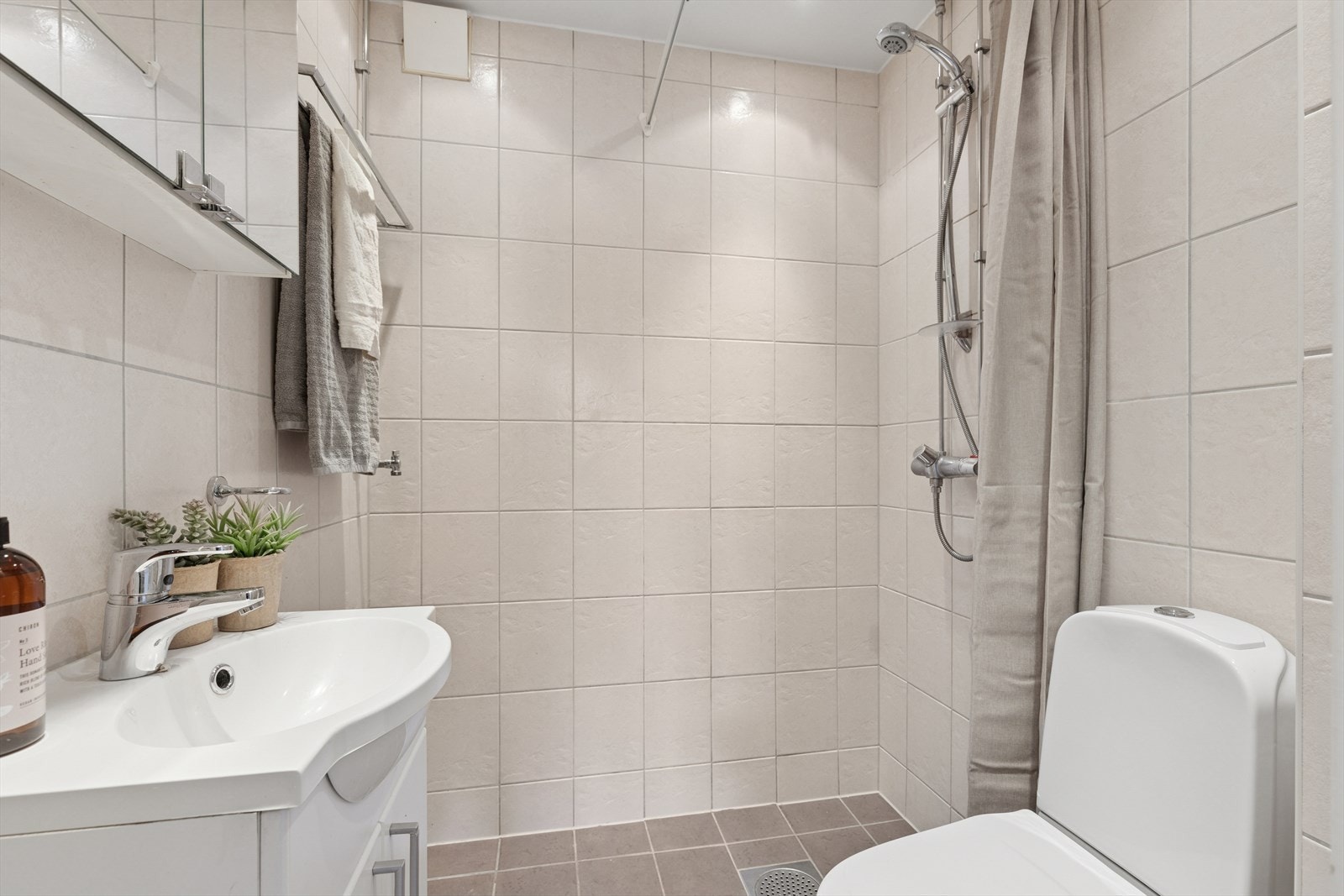 Innredningen inkluderer speilskap, servantskap, toalett, servant, dusjløsning og opplegg for vaskemaskin. Galleribilde