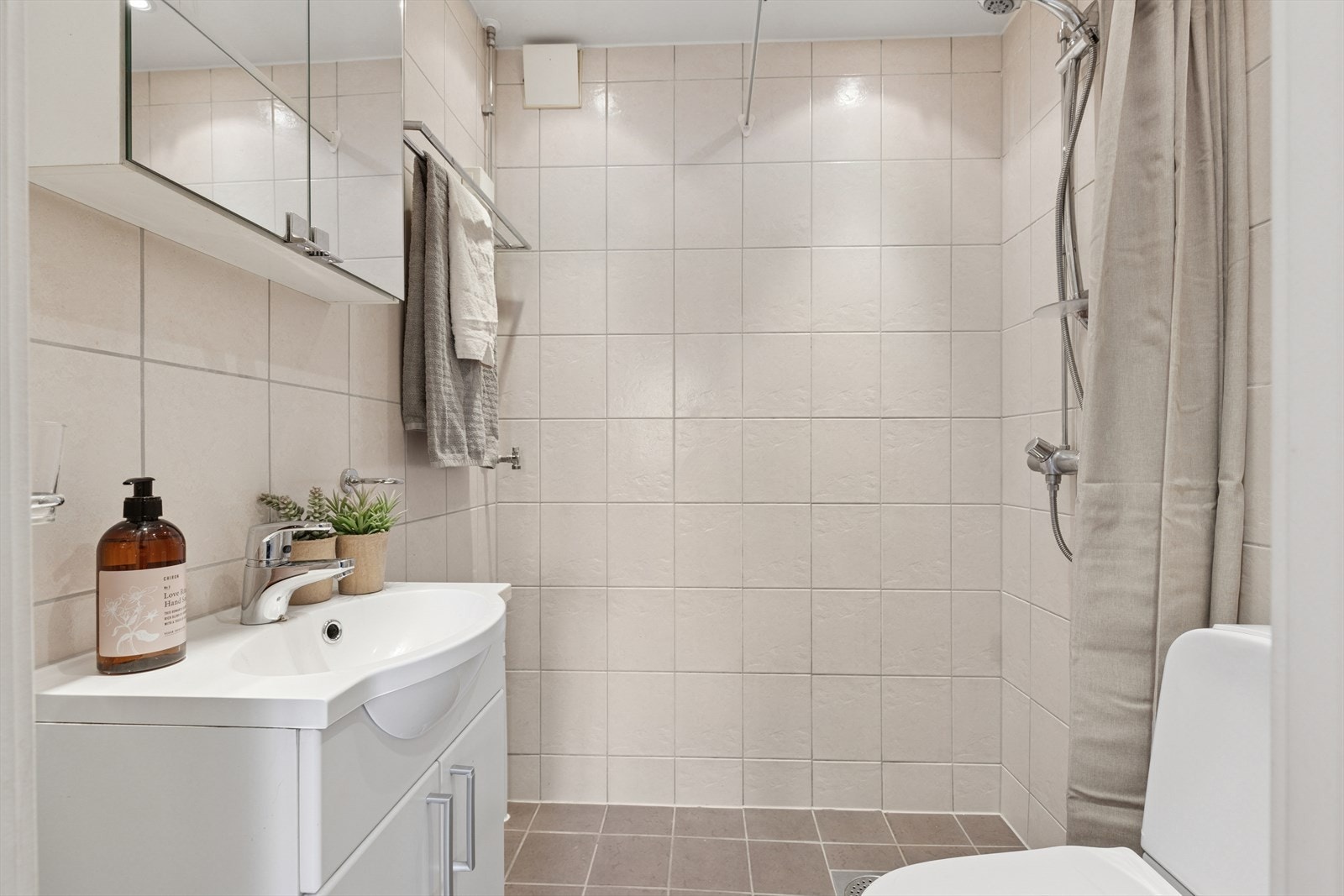 Baderom med en tidløs innredning med lyse fliser og funksjonelle løsninger som gir et rent preg. Galleribilde