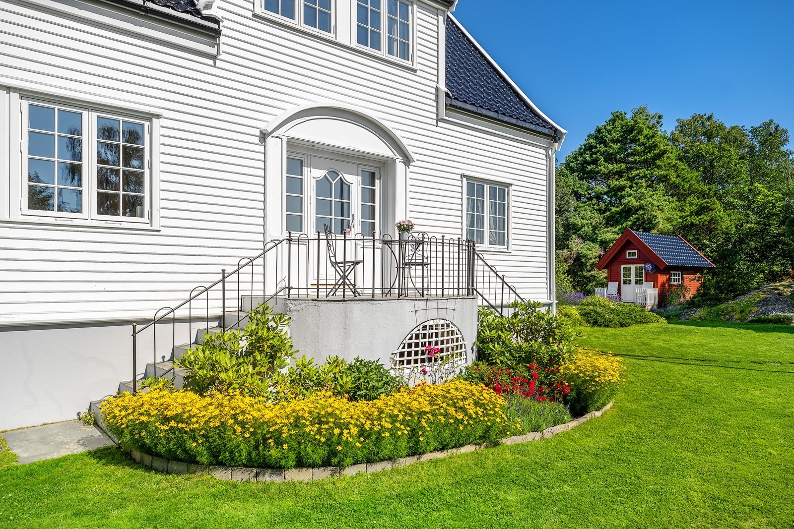 Tomten er opparbeidet med velstelte blomsterbed med planter av ulike fargespill Galleribilde
