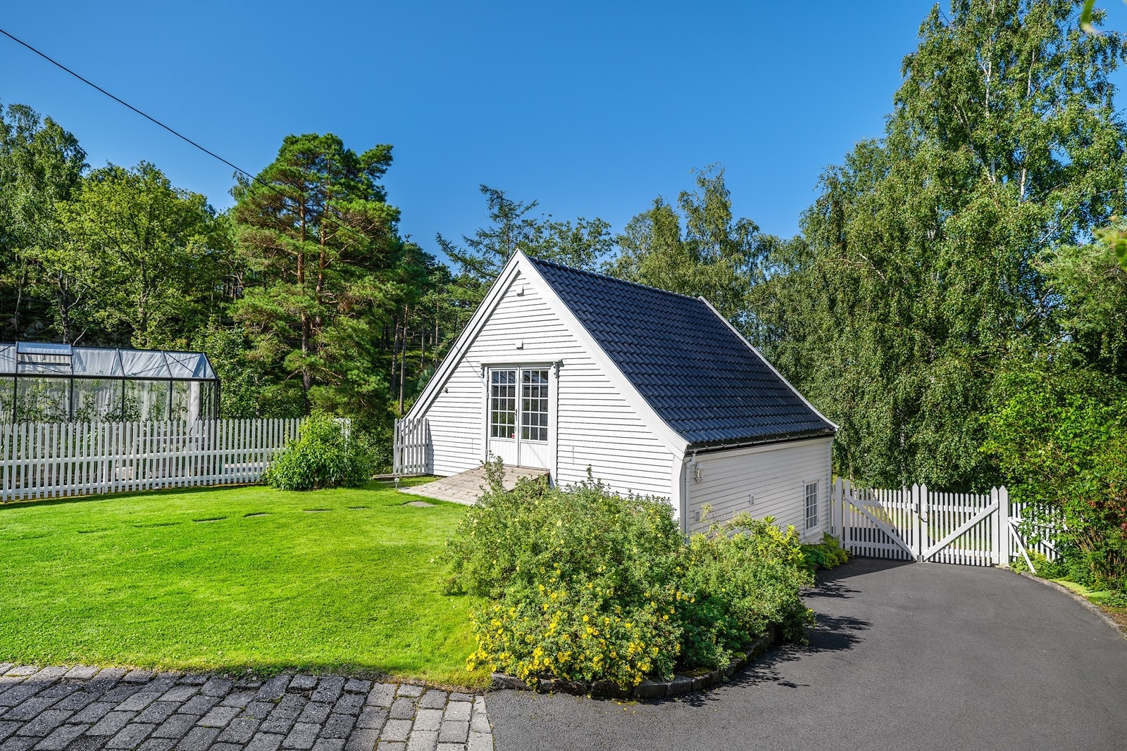 Garasjen har innredet loft/anneks i 2. etasje. Etasjen er innredet med 2 rom. Dobbel dør gjør det praktisk for evt. lagring av hagemøbler. Drivhus med vanningssystem beliggende bak gjerdet. Galleribilde