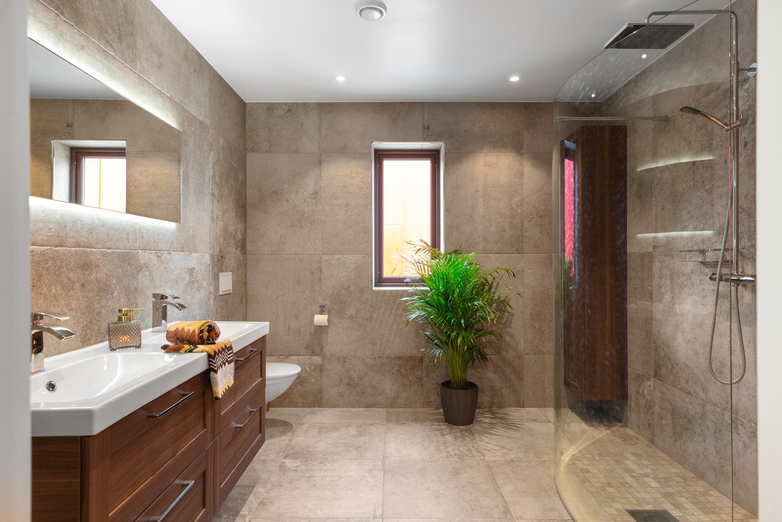 Badet er utstyrt med varme i gulv, innredning med servant, vegghengt toalett, dusjvegger av glass og dusjgarnityr på vegg. Galleribilde