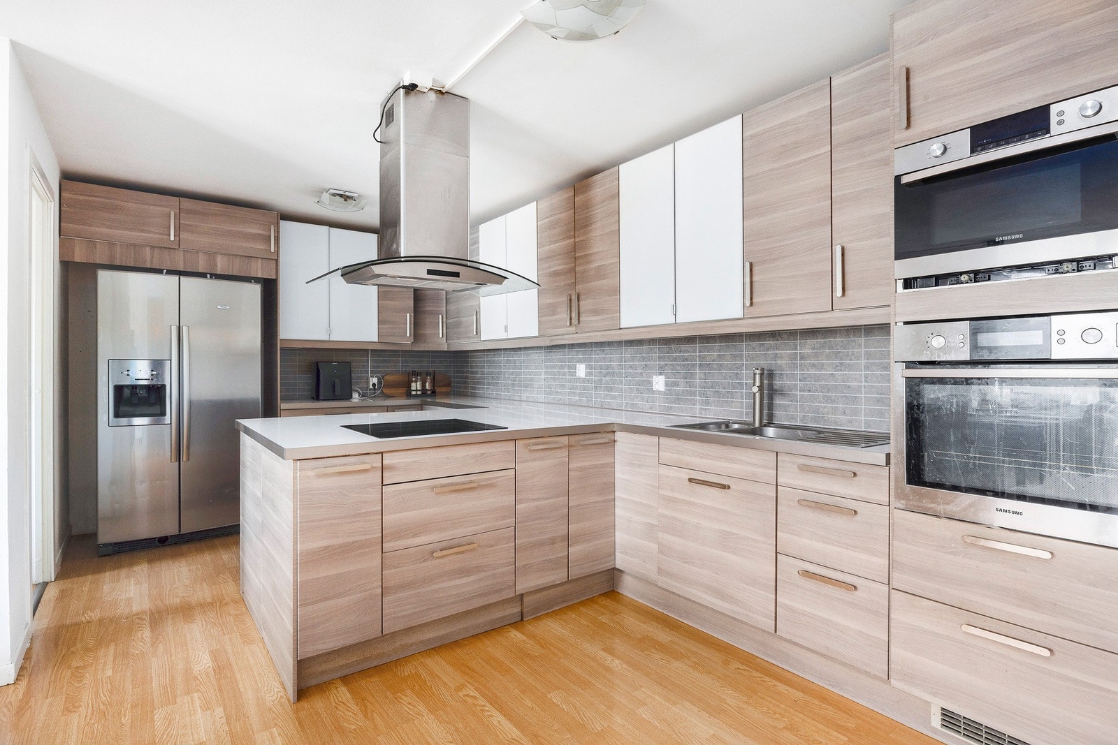 Kjøkkenet har en innredning med glatte fronter i lyse bruntoner, kombinert med enkelte hvite skap. Benkeplaten er i laminat, og det er integrerte hvitevarer som oppvaskmaskin, komfyr, platetopp og mikrobølgeovn. Galleribilde