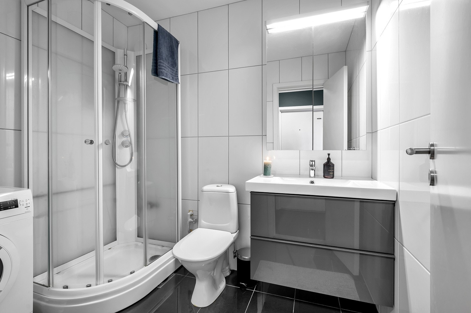 Flislagt bad med dusjkabinett, servant med underskuffer og opplegg til vaskemaskin Galleribilde