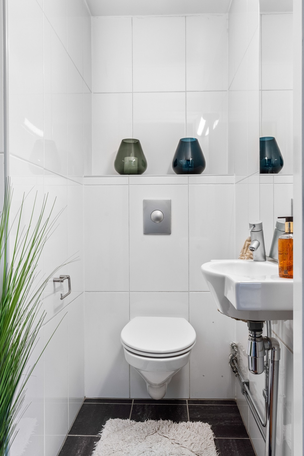 Wc-rommet har samme type fliser som badet, utstyrt med vegghengt toalett, enkel servant og lys over speilet. Galleribilde