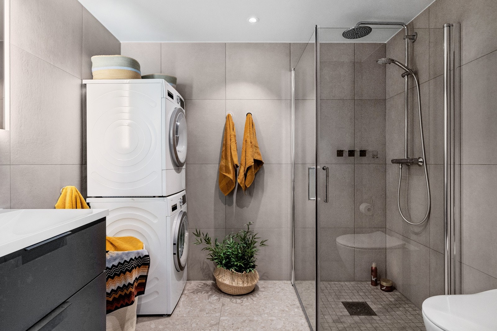 Helfliset baderom med tilknytning fra hovedsoverom med mørk innredning, veggmontert toalett, dusjhjørne og opplegg for vaskemaskin og tørketrommel. Galleribilde