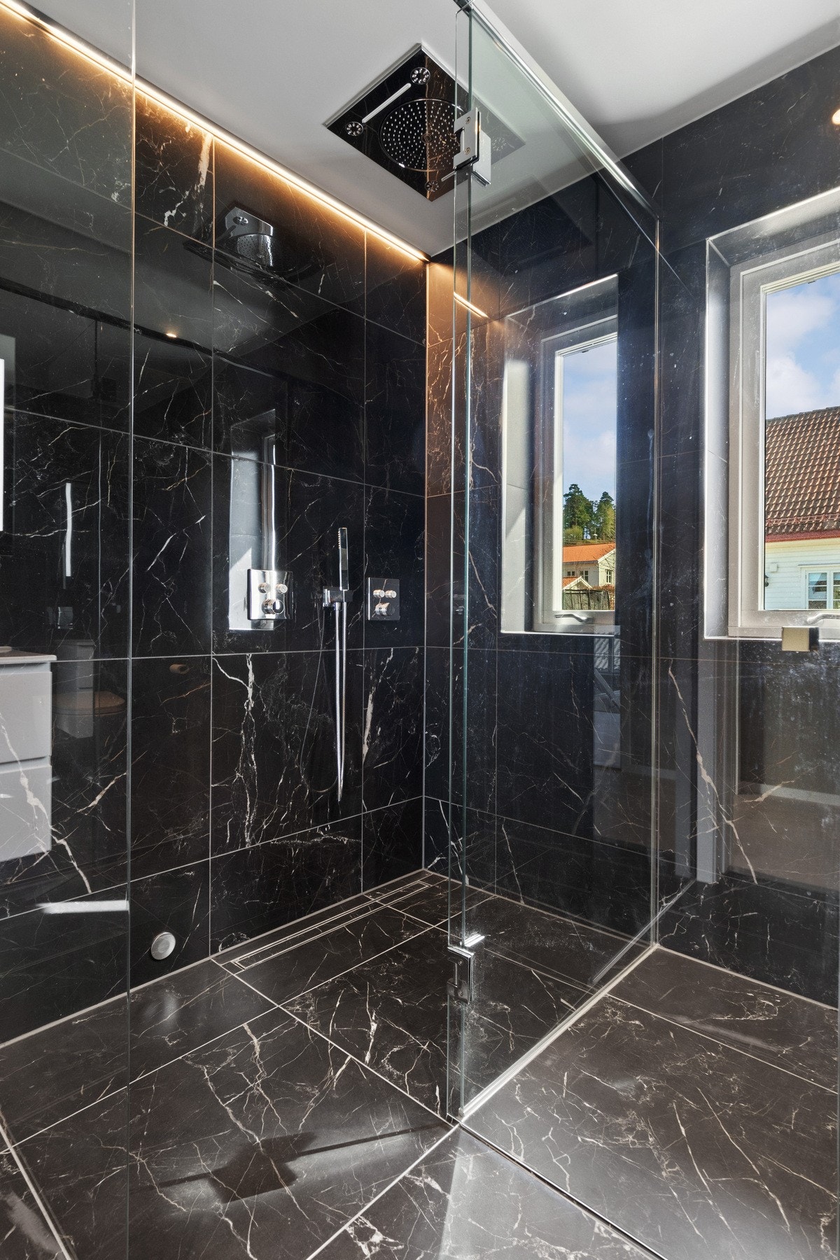 Dusjnisjen avgrenses av glassvegger med glassdør, og har også dobbel hånddusj, knappepanel, ledstripe og to flissatte slukrenner. Galleribilde