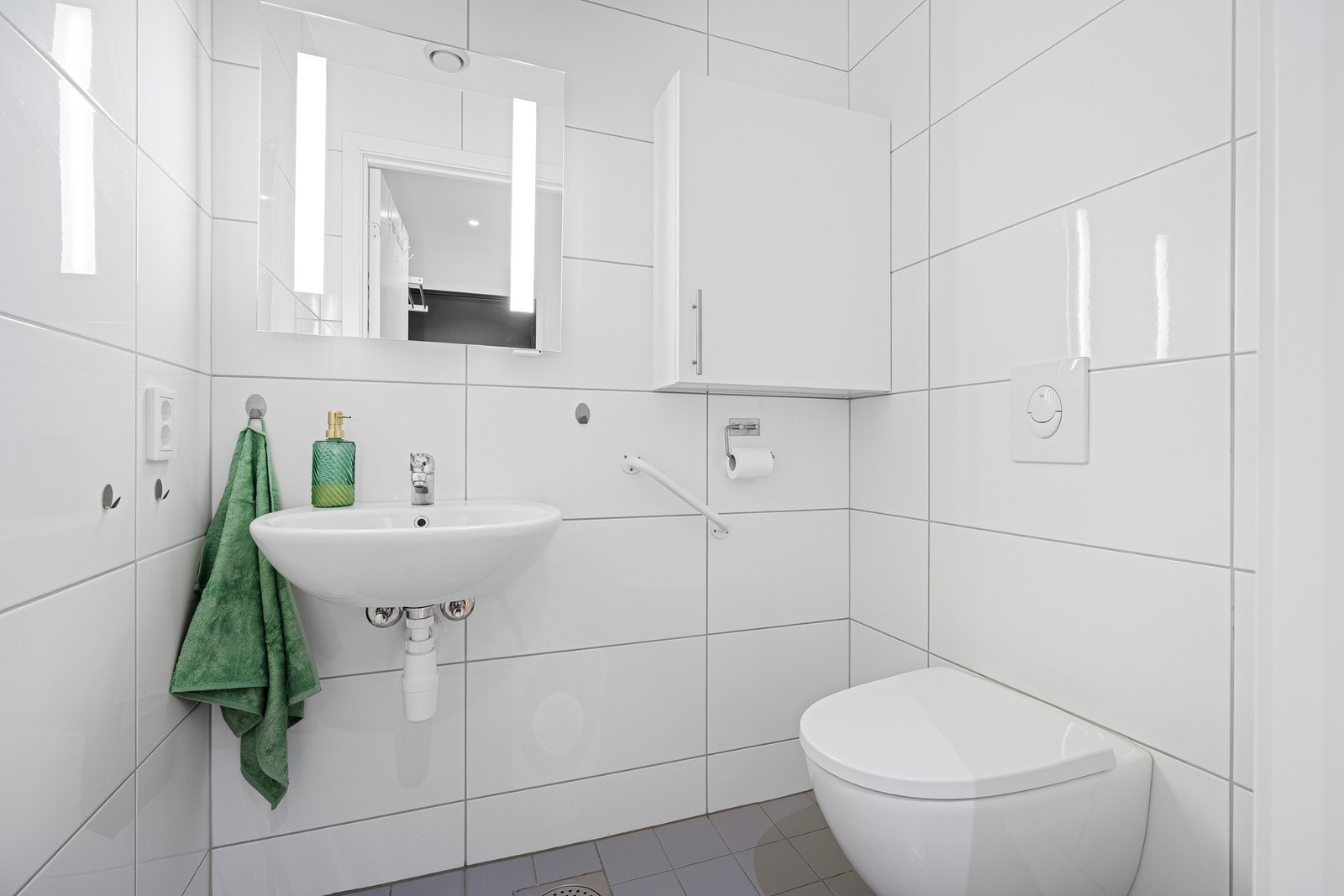 Fliselagt separat wc med vegghengt wc, servant, overskap og speilskap med lys. Galleribilde
