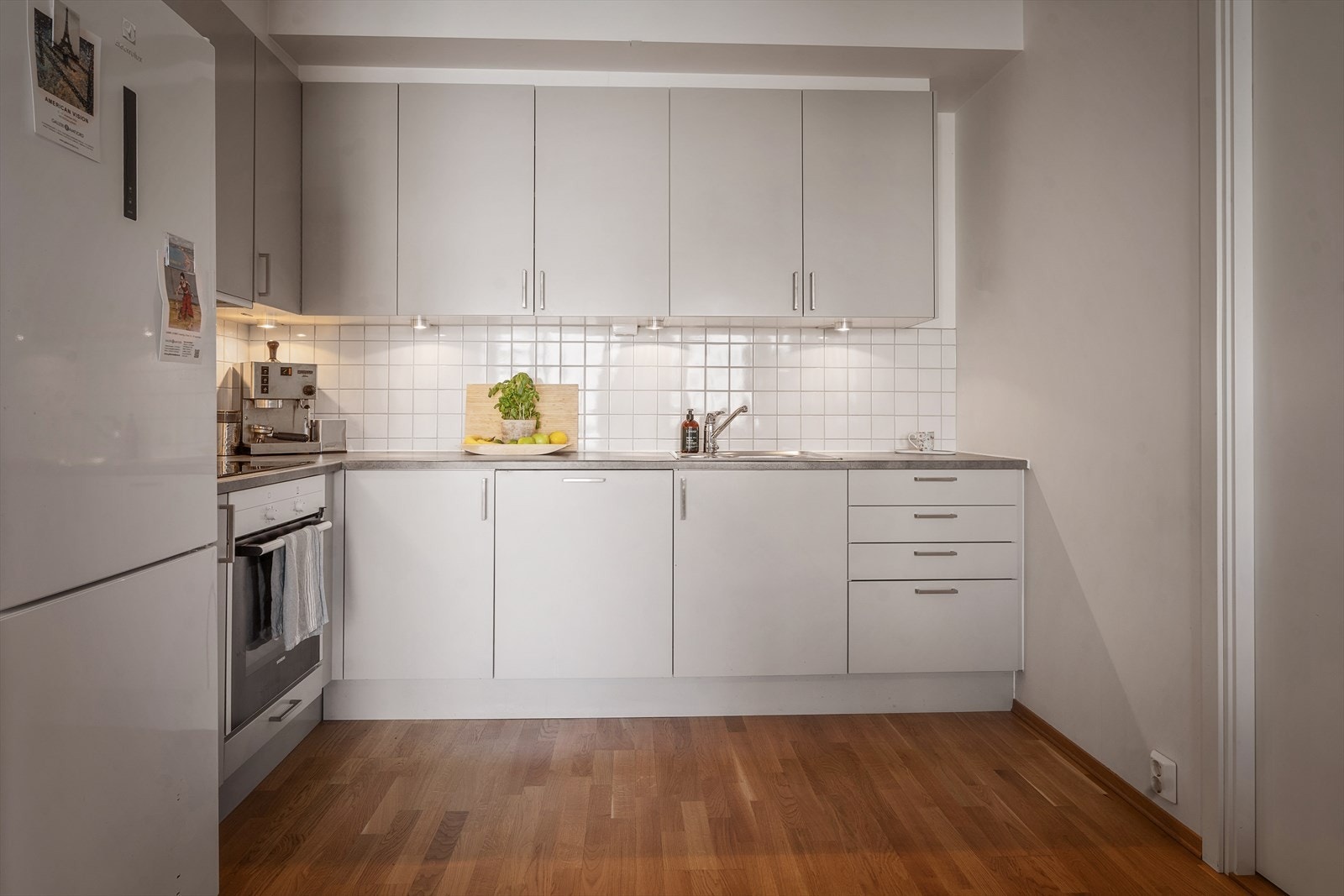 Stilrent kjøkken fra byggeåret med hvite, glatte fronter, fliser på bakvegg og benkeplate i laminat. Galleribilde