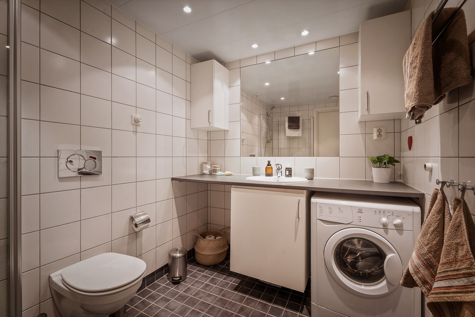 Badet er utstyrt med vegghengt toalett, dusjhjørne, baderomsinnredning med under-/overskap og opplegg for vaskemaskin og tørketrommel. Galleribilde