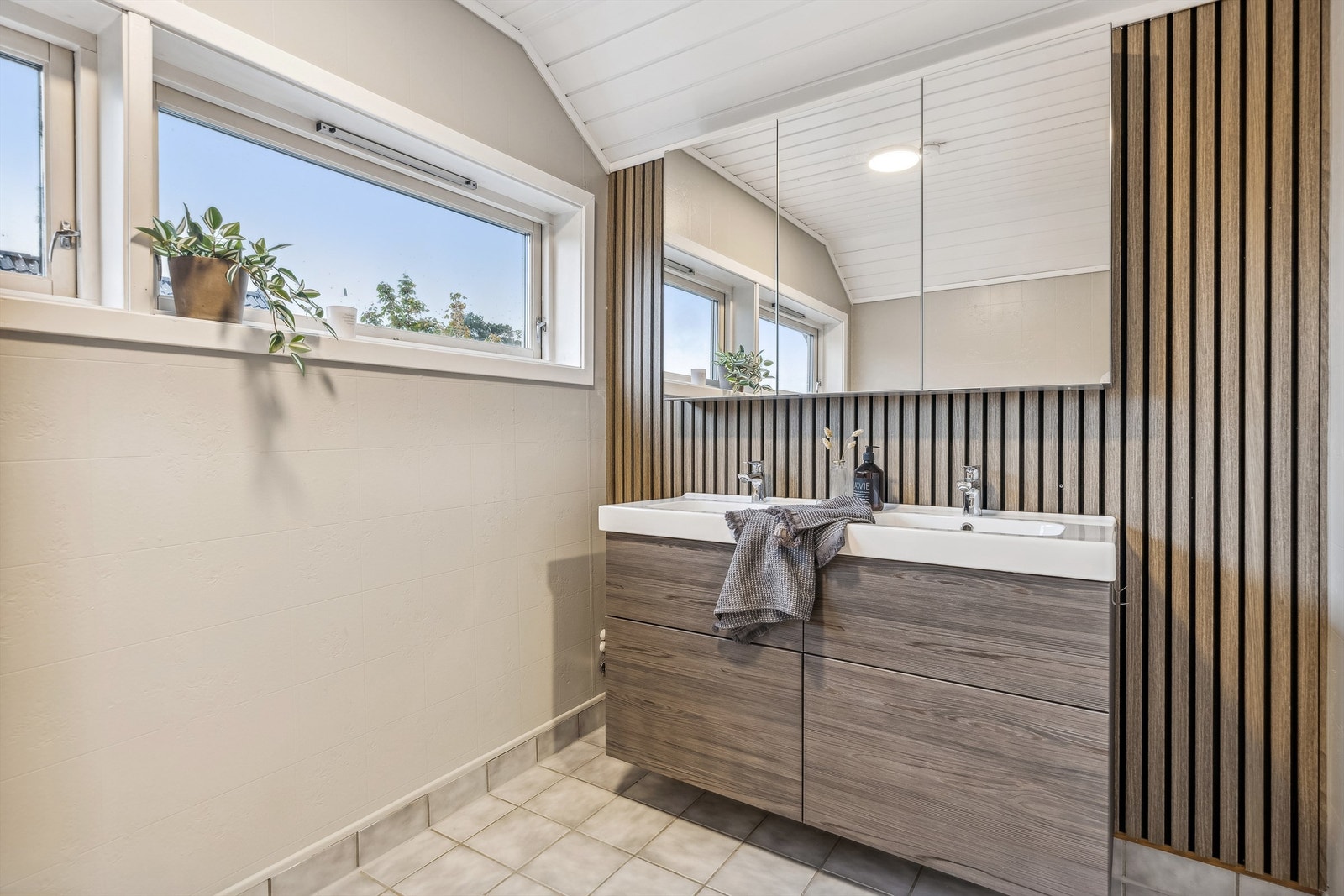 Pent bad/vaskerom med flislagt gulv. Badet ble oppgradert med overflatebehandling på veggflater, nytt toalett, ny servantinnredning og spilevegg i 2020 Galleribilde