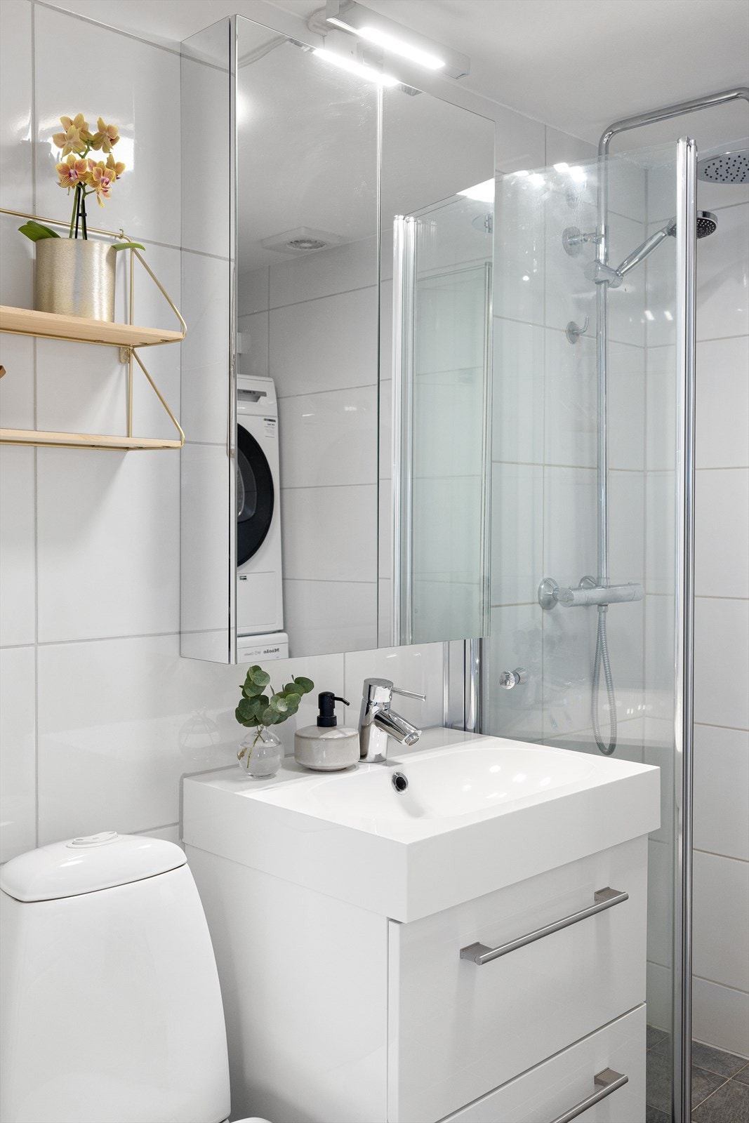 Badet er innredet med helstøpt servant i innredning med skuffer. Speilskap med belysning. Toalett. Dusj med takdusj og hånddusj, samt innfellbare glassdører Galleribilde