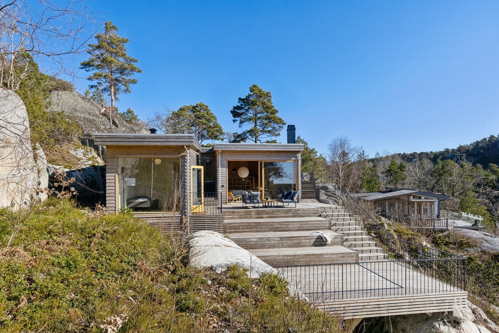 Hytte og anneks er nøysomt plassert på pilarer inn i terrenget Galleribilde