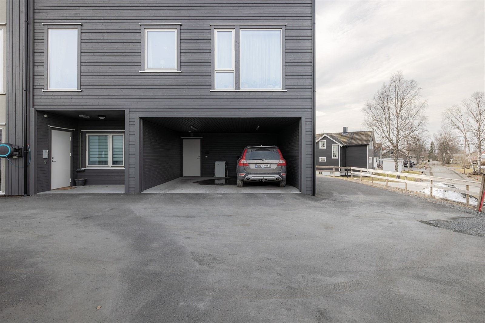 Overbygget inngangsparti. Asfaltert gårdsplass og carport like ved inngangen. Det er klargjort for elbil lader i carport Galleribilde