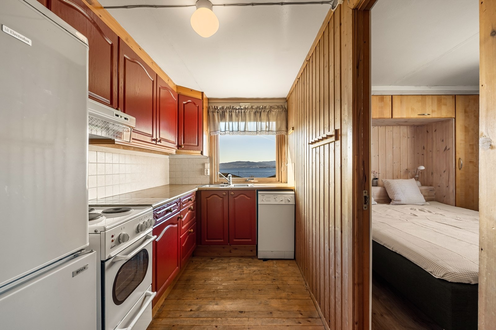 Kjøkkenventilator med avtrekk ut og frittstående hvitevarer som kjøle/fryseskap, vaskemaskin og komfyr. Galleribilde