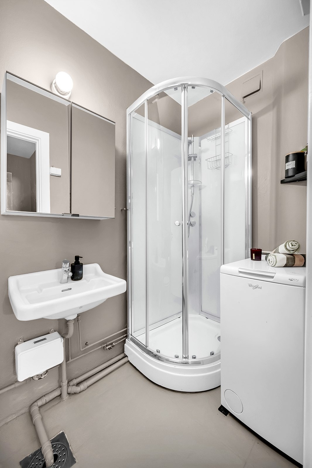 Innredningen består av gulvstående toalett, vegghengt servant og vegghengt speilskap over servant. Videre er det dusjkabinett med skyvedører av glass. Opplegg for vaskemaskin. Galleribilde