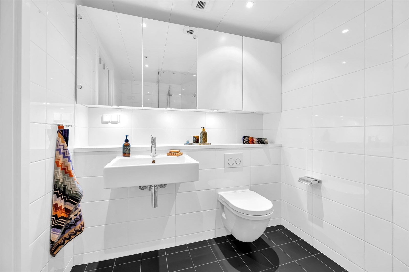 Badet er innredet med vegghengt toalett, servant nedfelt i innredning og dusjhjørne med svingbare glassdører. Galleribilde