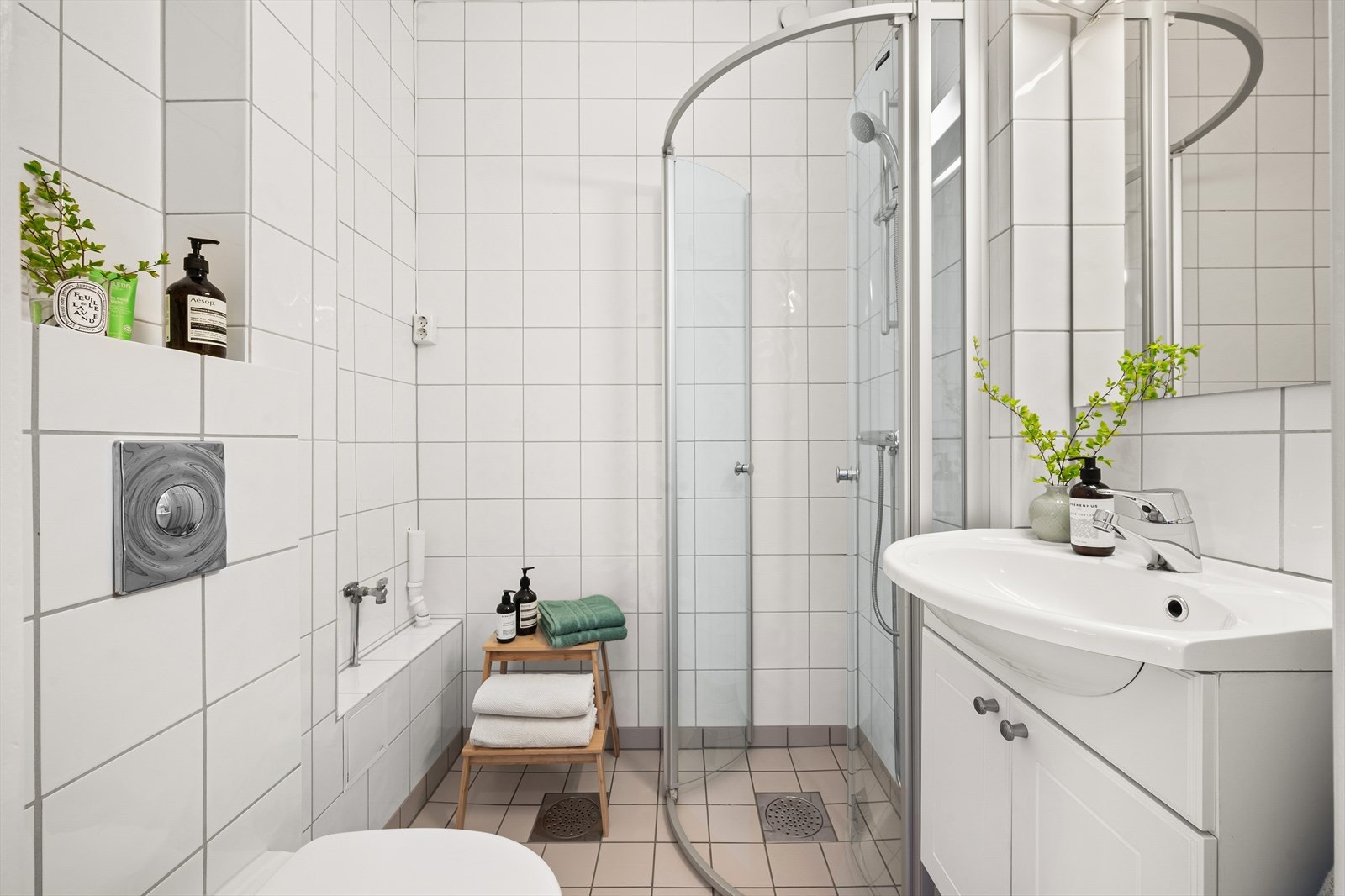 Baderommet er innredet med veggmontert klosett, servant skap med glatte, folierte fronter, speil og dusjhjørne med buede svingdører. Galleribilde