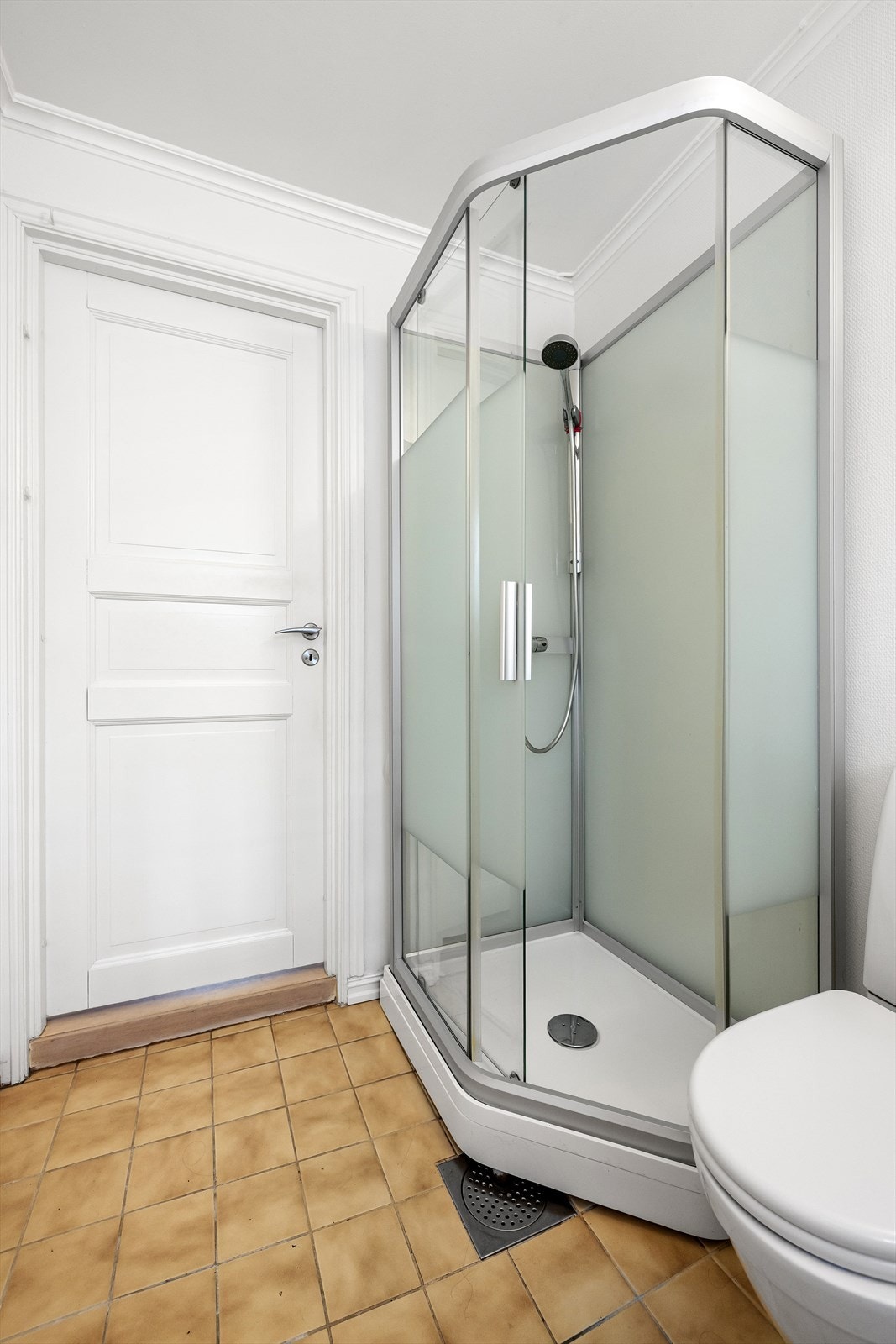 Her er det fliser på gulv med varmekabler og et fall på 2 cm fra dørkarmen til sluket. Veggene har strie, og taket er malt og slett. Galleribilde