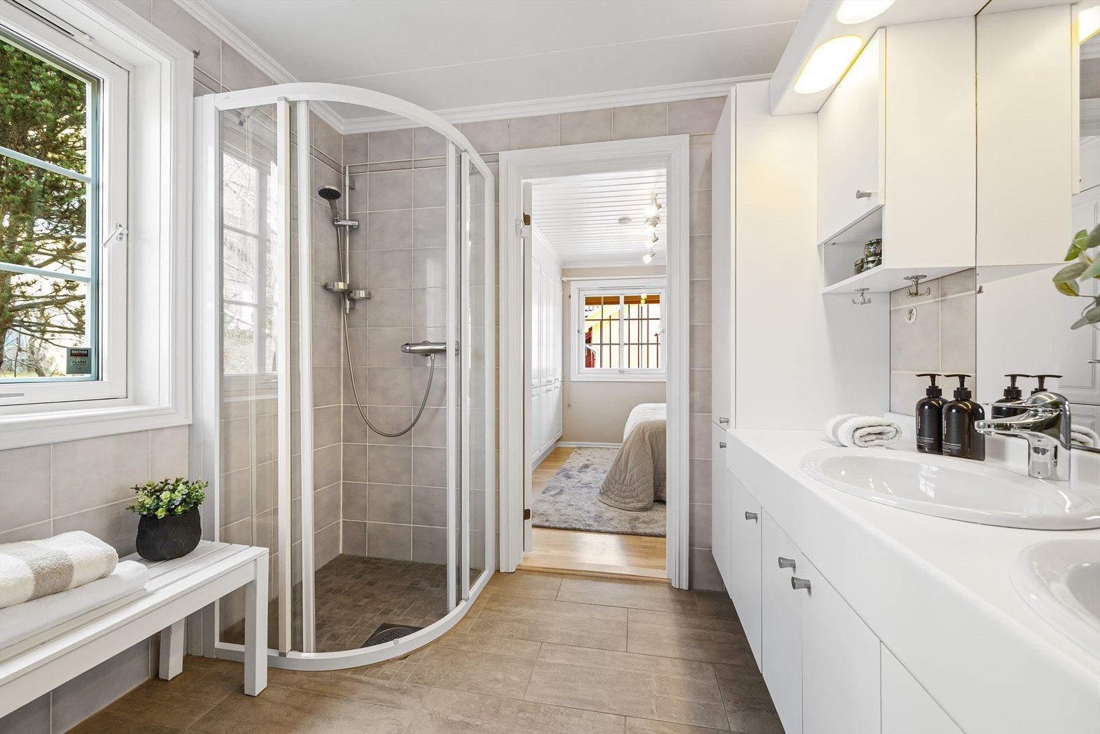 Rommet er utstyrt med 2 nedfelte servanter, flere skuffer og skap. Det er et stort speil over vaskene, gulvmontert toalett og bidé samt buede dusjvegger/hjørne med skyvedører. Galleribilde