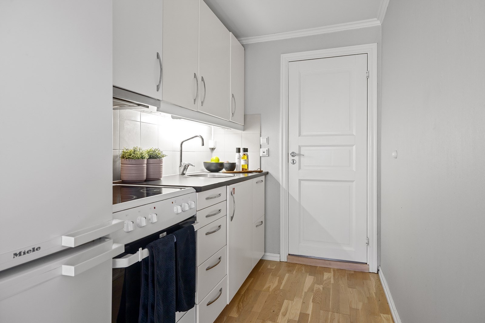 Kjøkkeninnredning med glatte fronter og overskap. Benkeplaten er i laminat med en nedfelt metallvask og ettgreps blandebatteri. Kjøkkenet har en avtrekksvifte med kullfilter (IKEA). Galleribilde