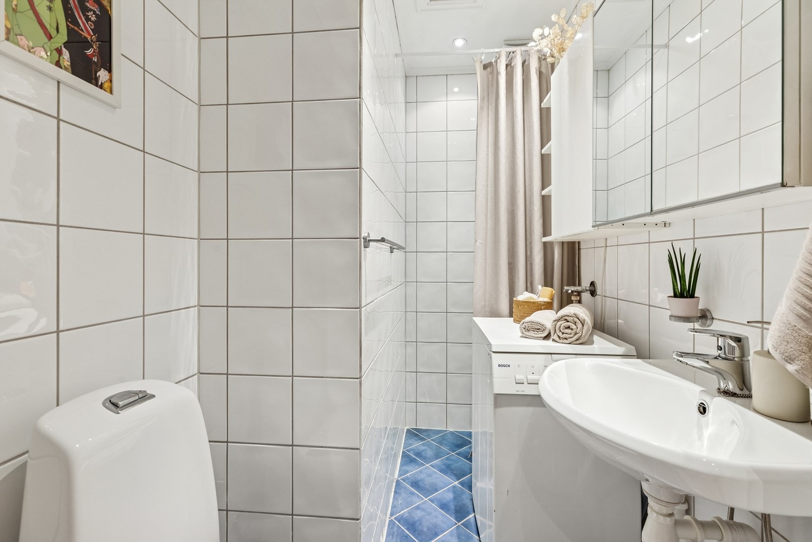 Rommet er utstyrt med dusj med forheng, klosett, servant, opplegg for vaskemaskin og baderomsinnredning med overskap og speilskap. Dagens eier bekostet nytt klosett i 2024. Galleribilde