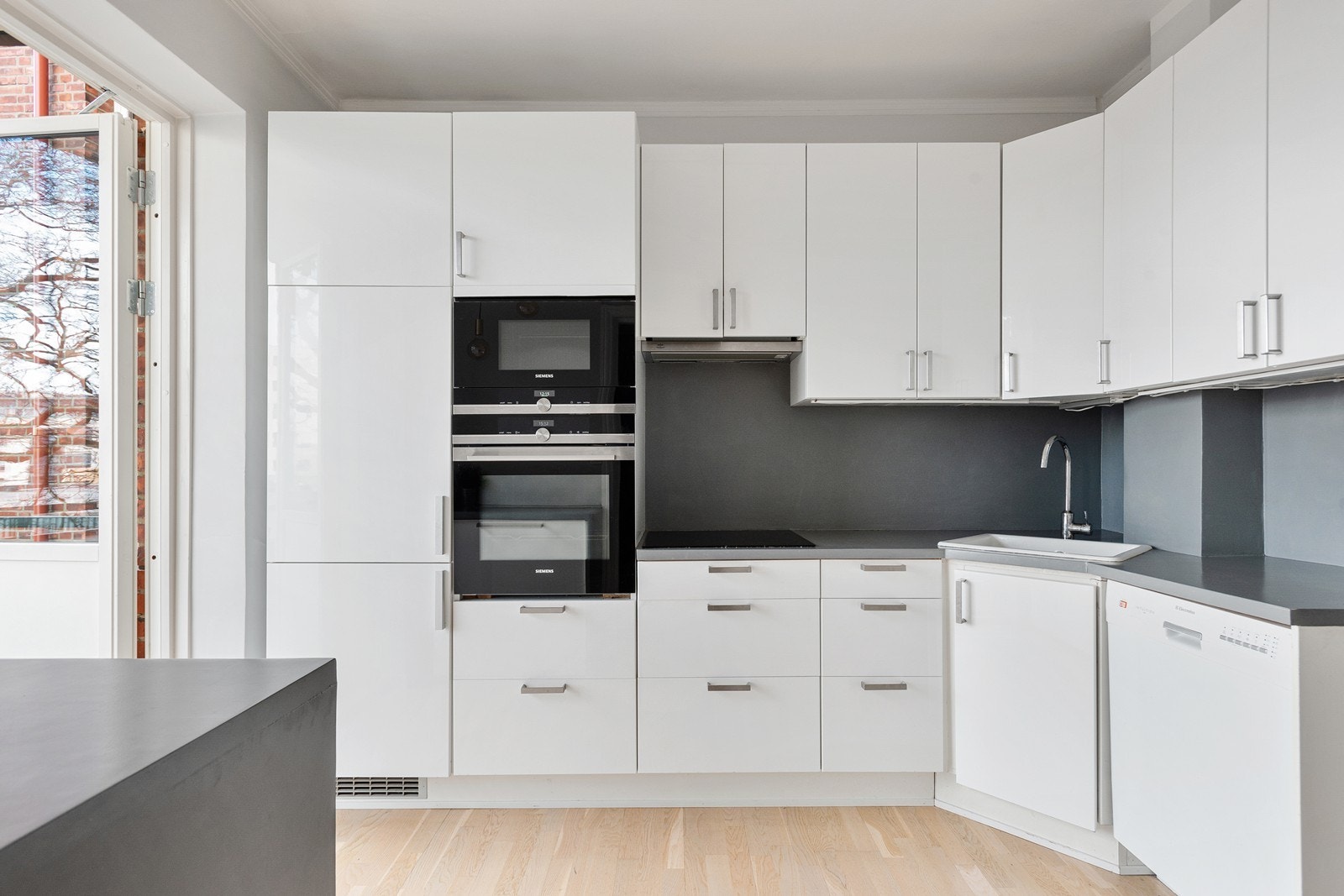 Lekkert kjøkken med benkeplate bestående av tre behandlet med mikrosement, nedfelt vask av porselen og hvitevarer som platetopp, stekeovn, mikrobølgeovn, oppvaskmaskin og kjøleskap/frys Galleribilde